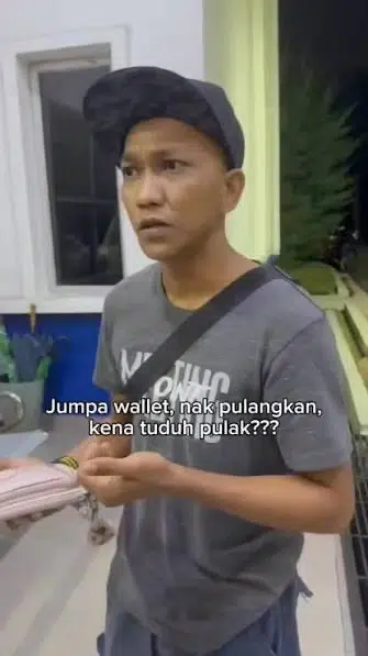 Man in a cap and gray shirt stands in a kitchen, holding a wallet and looking surprised; subtitles mention returning a found wallet in Indonesian.